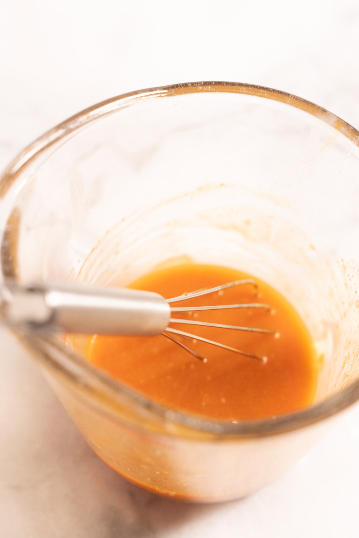 Hot honey sauce in measureing cup with whisk.