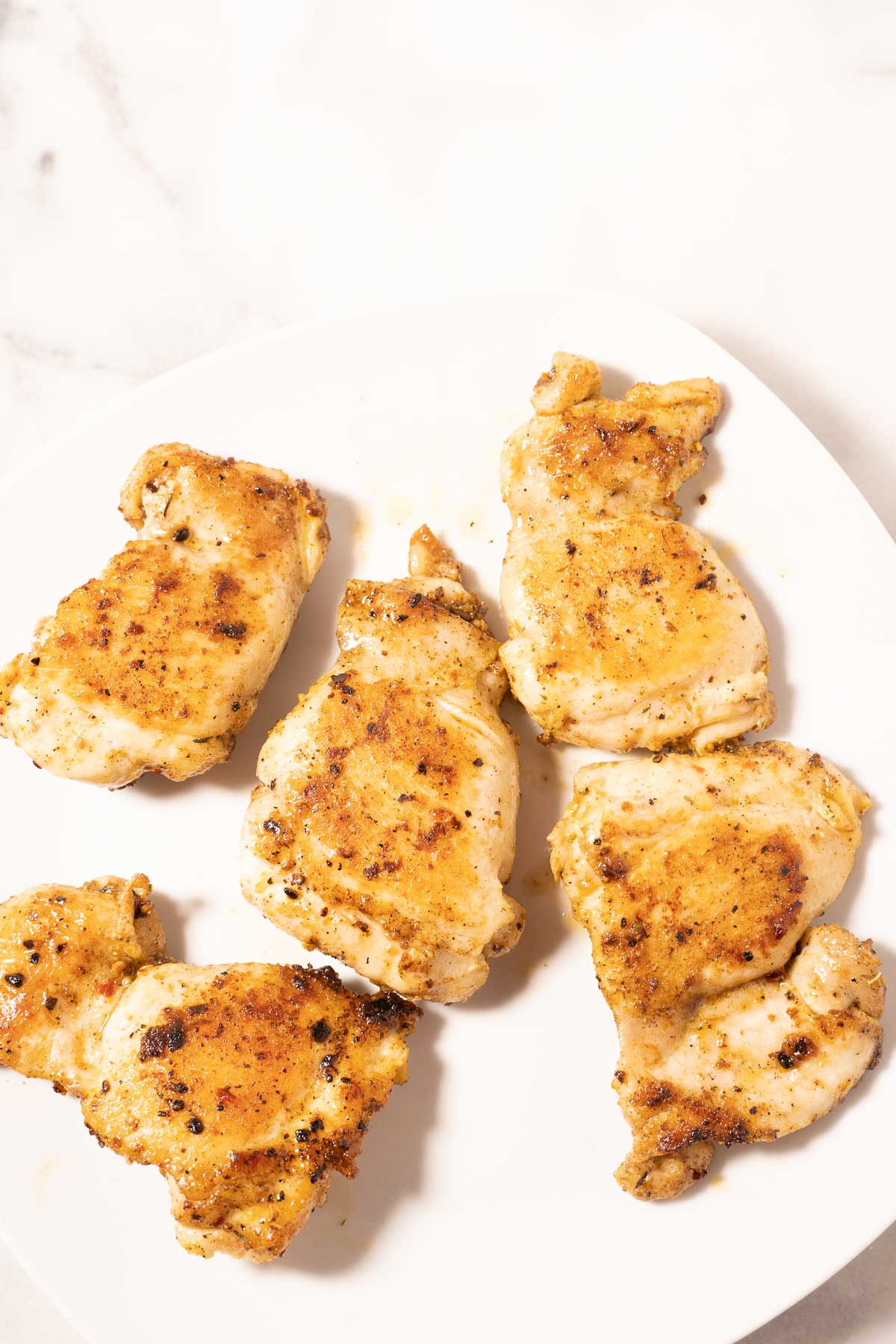 Pan fried seasoned chicken thighs on plate.
