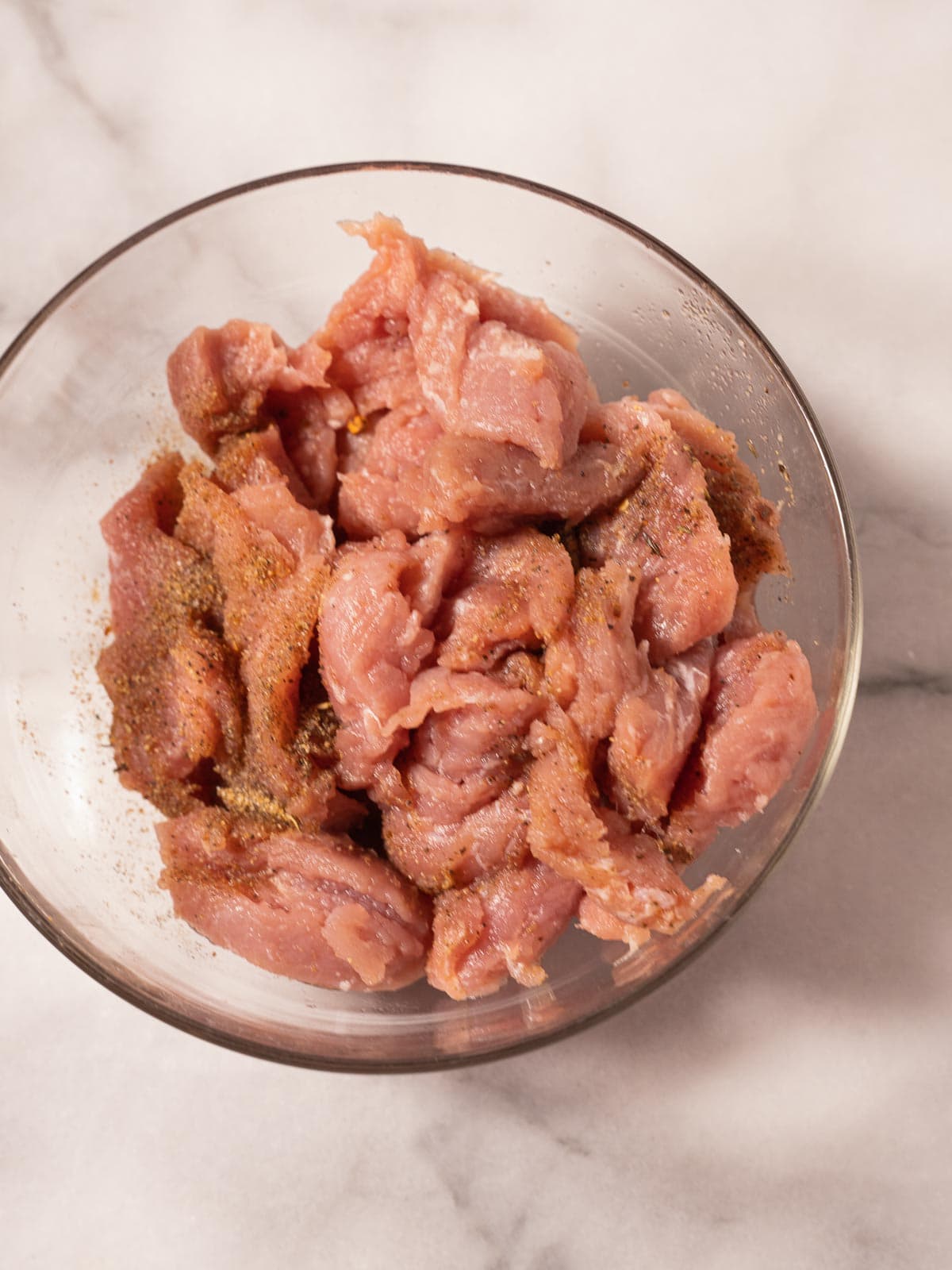 Seasoned sliced pork tenderloin in a glass bowl.