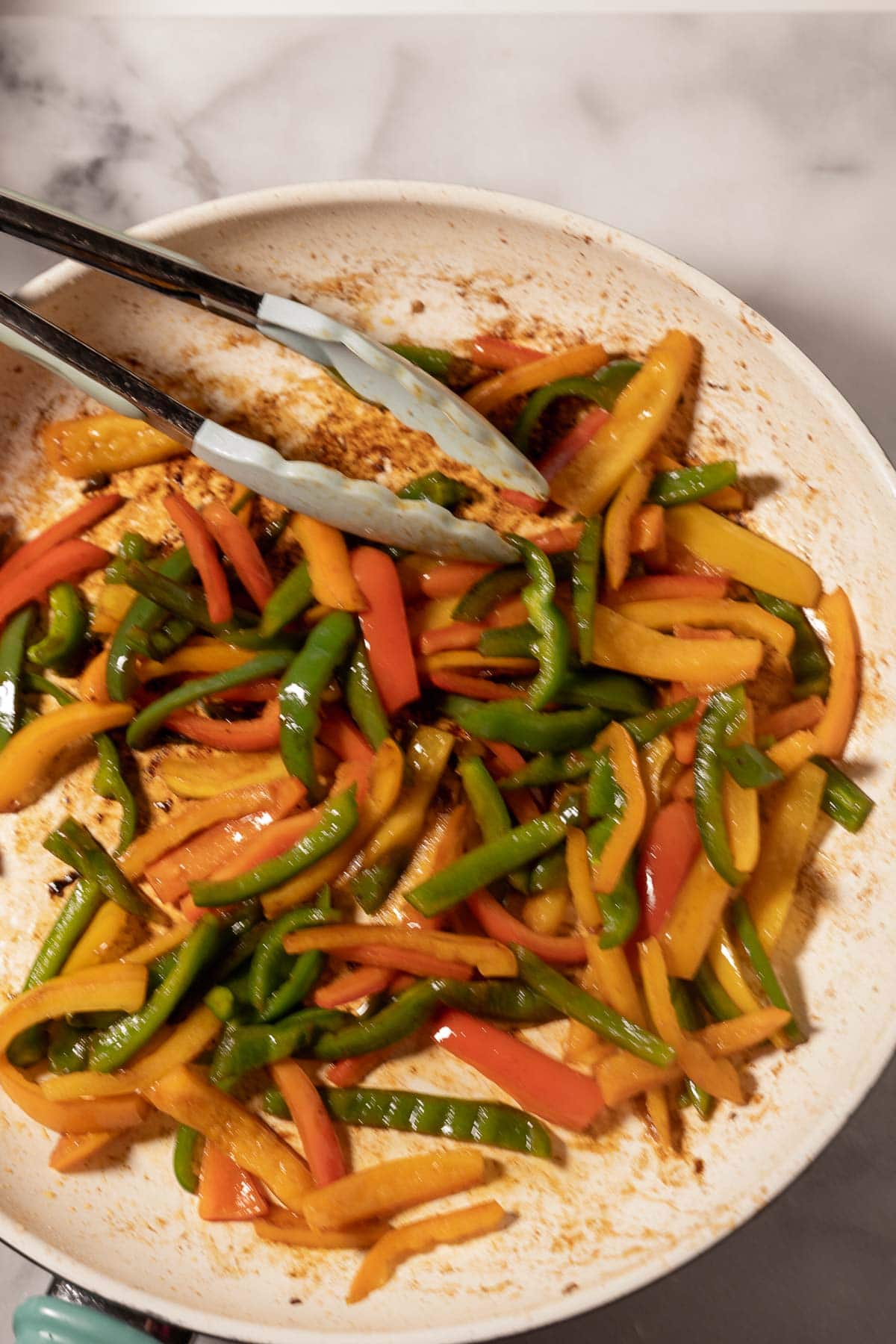 Stir fried red, yellow, green pepper slices in skillet.