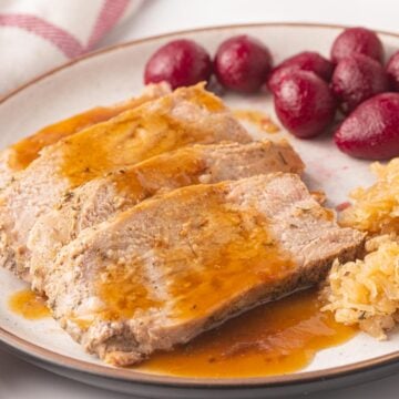 Slices of pork tenderloin with gravy, sauerkraut and beets on a plate.