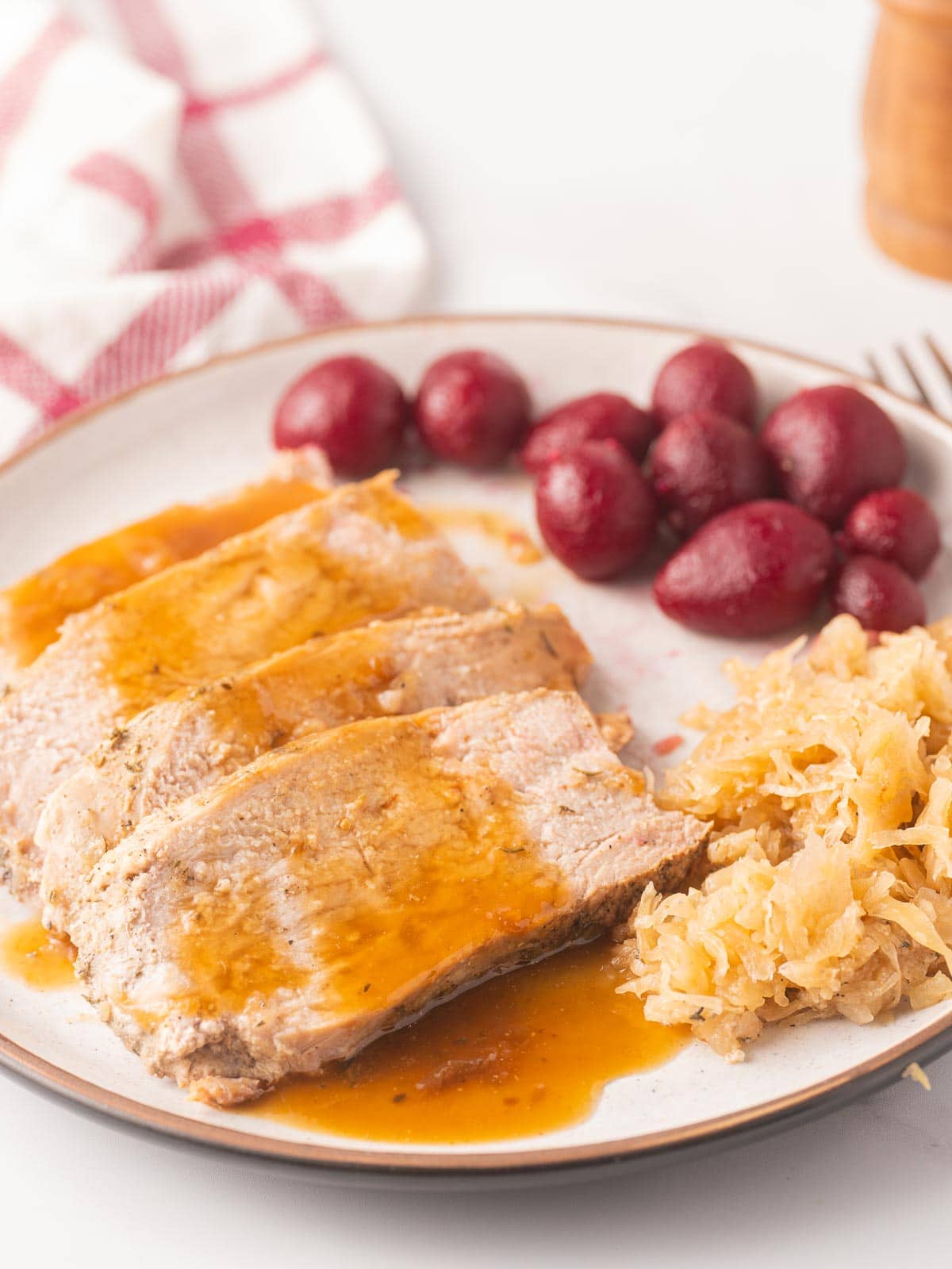 Sliced pork tenderloin with gravy, sauerkraut and beets on plate.