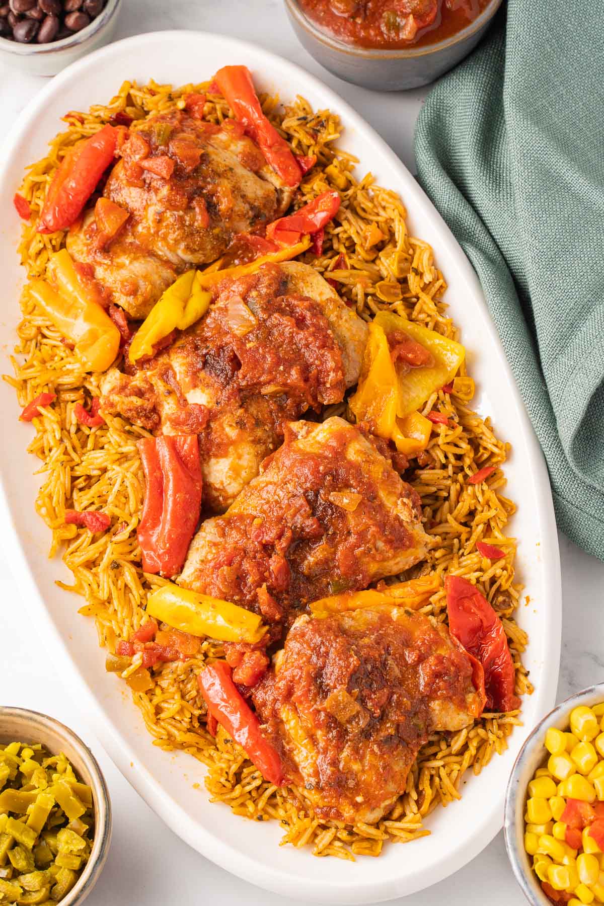 Salsa chicken with peppers over yellow rice on white platter with black beans and corn.
