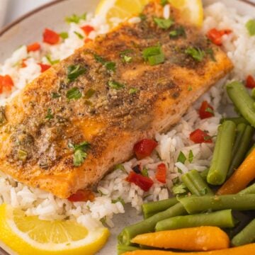 Blackened salmon fillet, rice, green beans, carrots, lemon slices on plate.