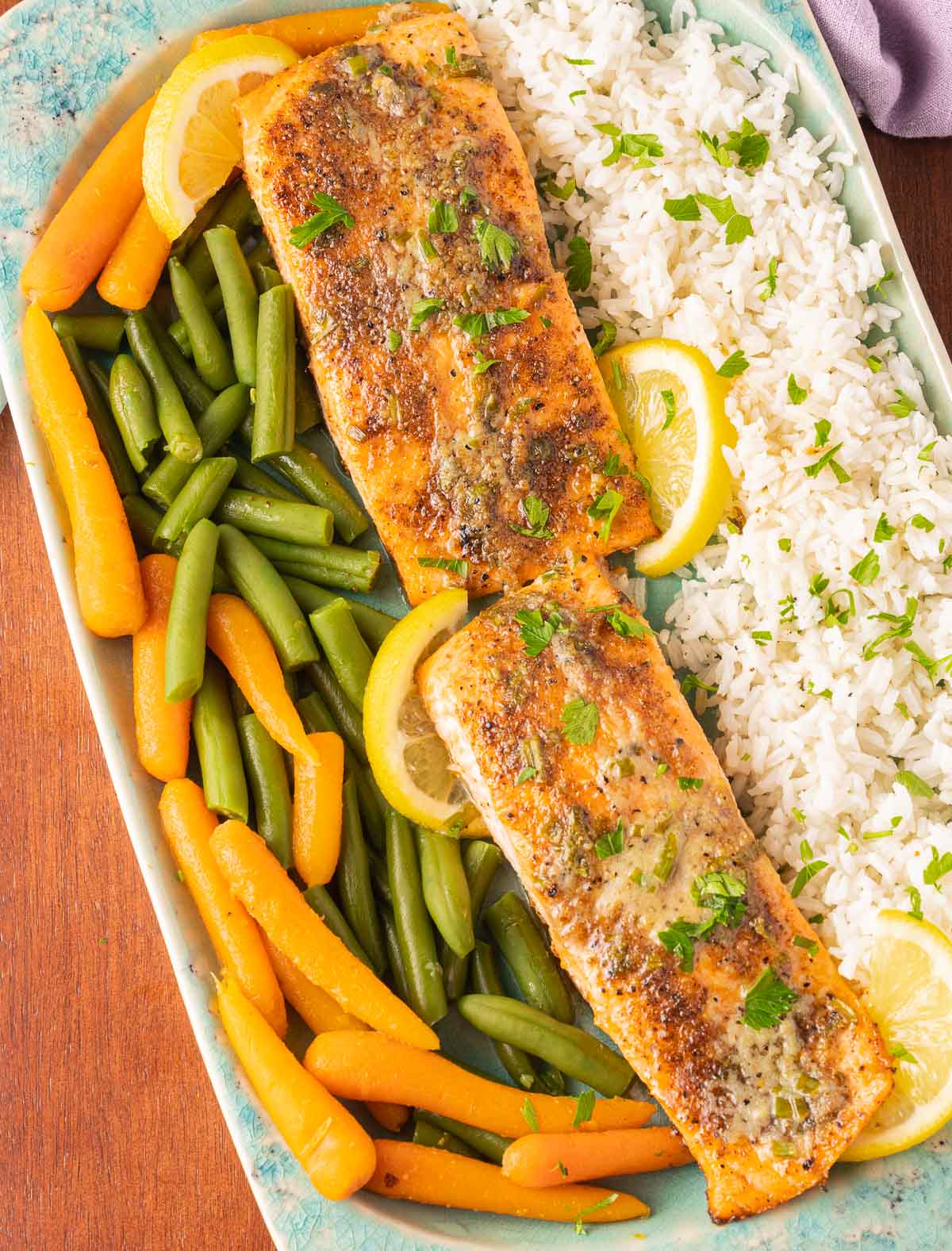 Baked Blackened Salmon fillets, rice, lemon slices. green beans, carrots on green platter.