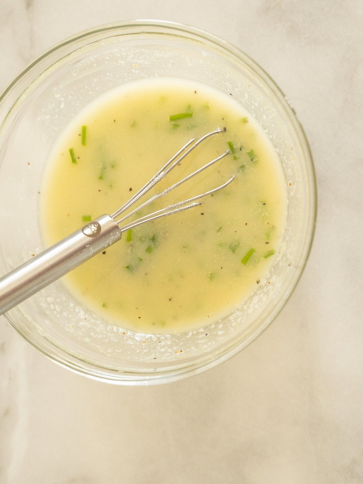 Lemon chive sauce in bowl with whisk.