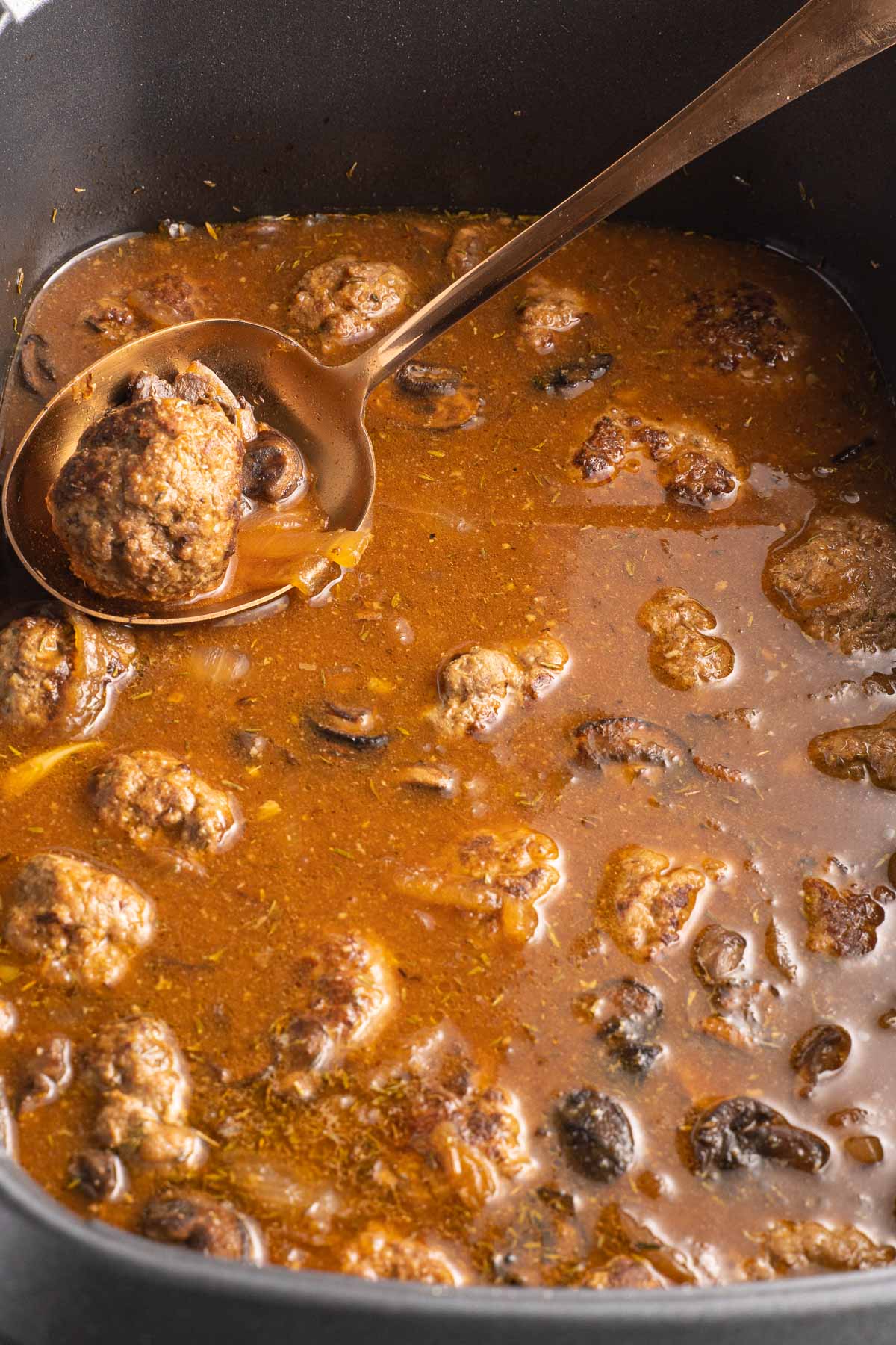Salisbury Steak meatballs simmering in gravy in slow cooker.