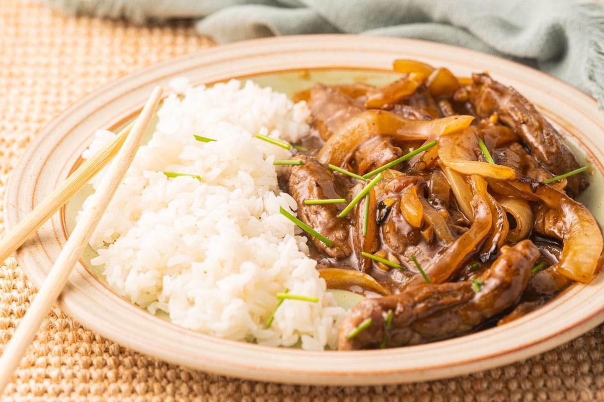 Beef and onion stir fry with rice on plate.