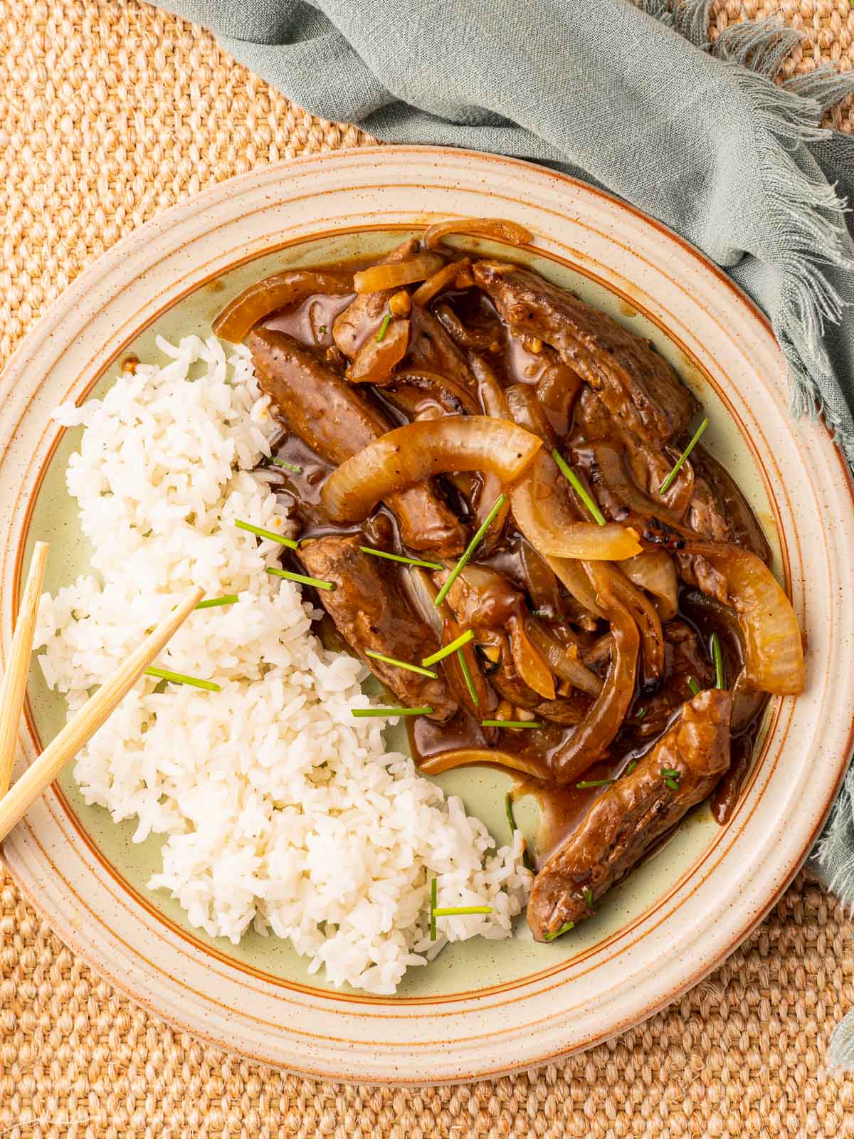 Beef and onion stir fry with rice and chopsticks on plate.