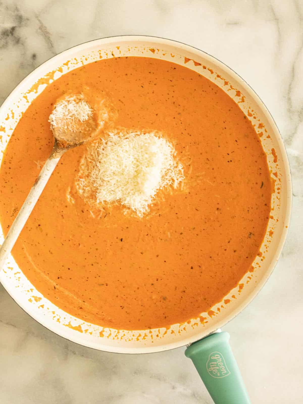 Pink sauce with parmesan cheese and wooden spoon in skillet.