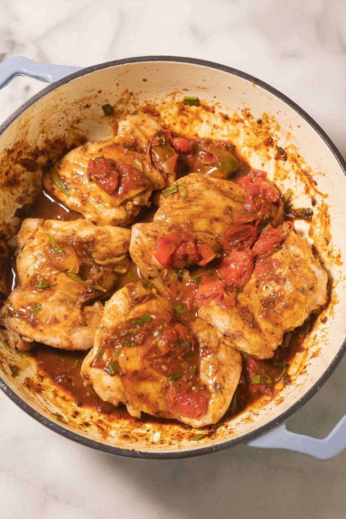 Boneless chicken thighs with burst tomato sauce in pot.