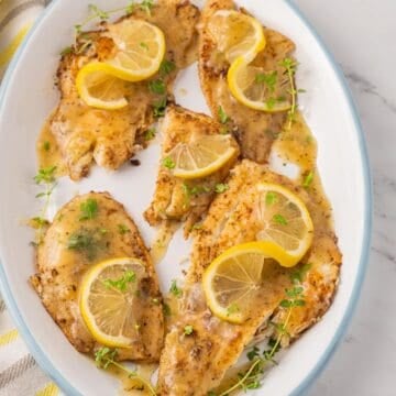 Flounder Francaise fillets on white platter with lemon and thyme .