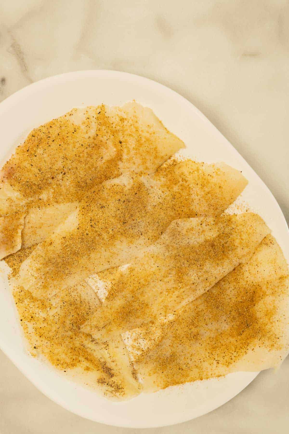 Seasoned flounder fillets on white platter.
