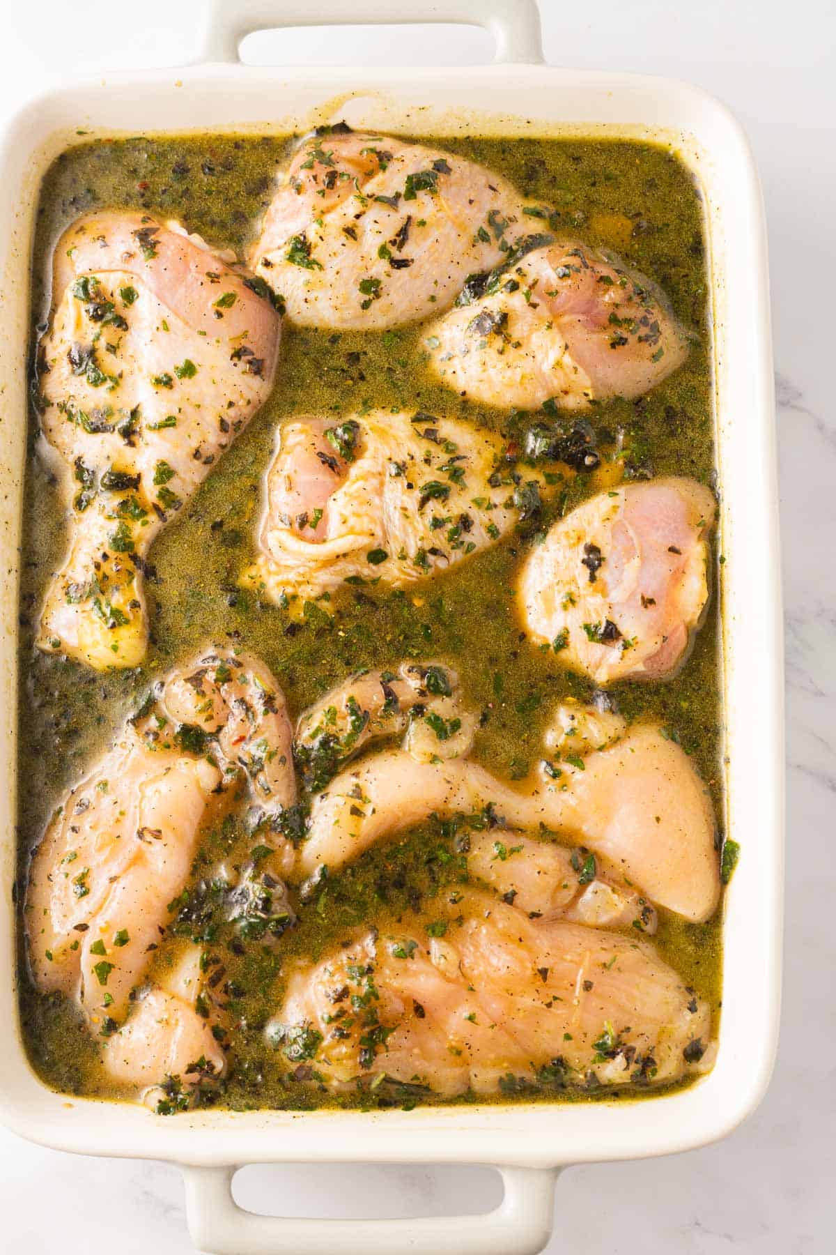 Basil marinade with chicken legs and boneless breasts in casserole dish.