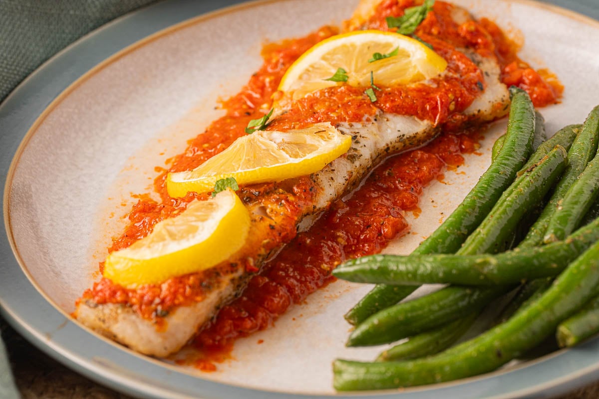 Baked Pollock and red pepper sauce with green beans on plate.