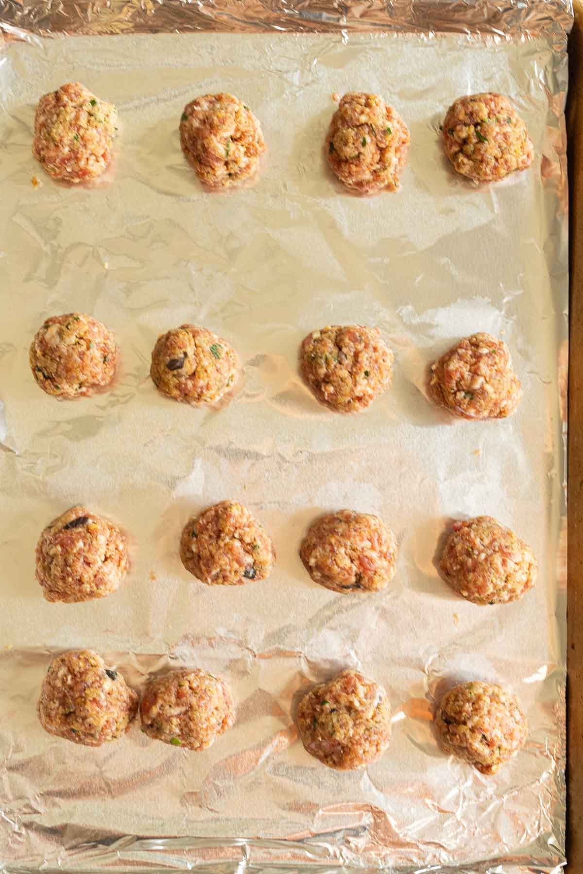 Raw sausage meatballs on foil on baking sheet.