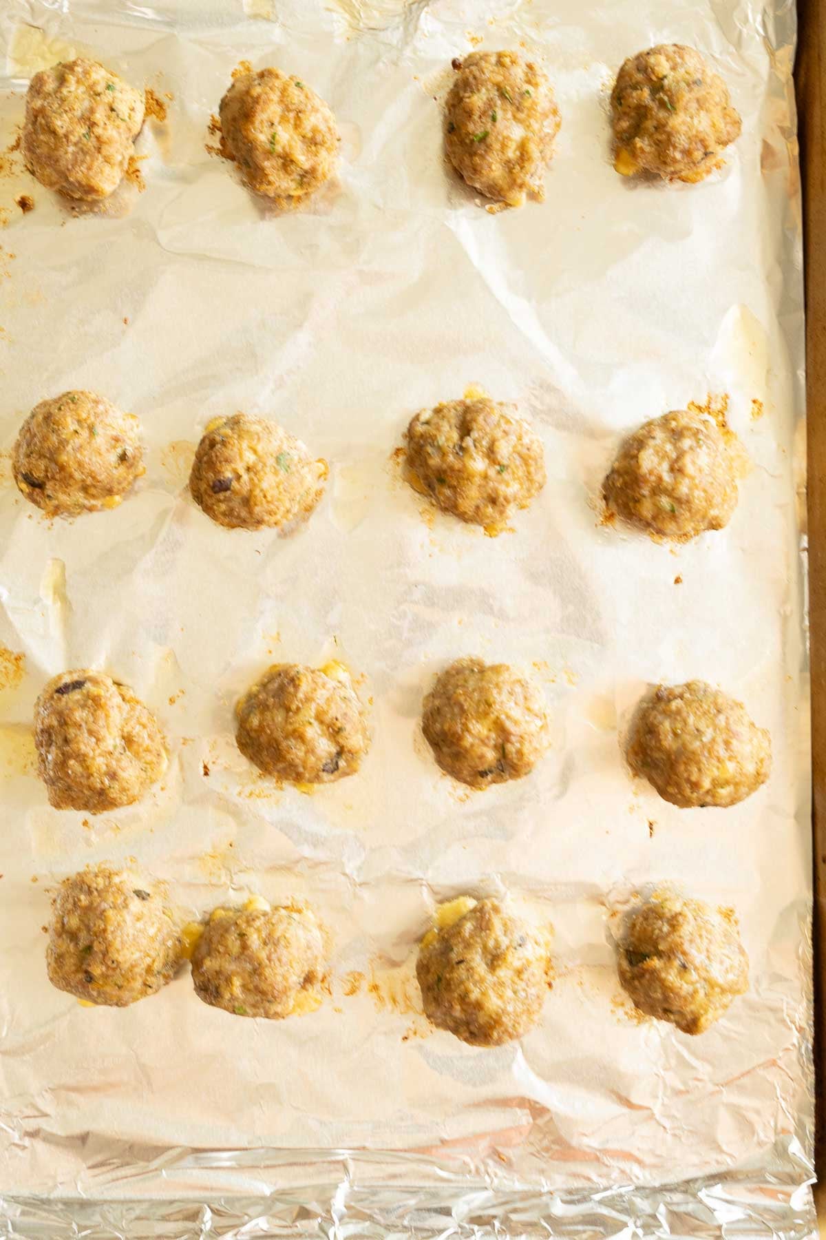Baked sausage meatballs on foil on baking sheet.