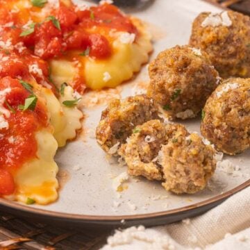 baked sausage meatballs with ravioli and sauce on plate.