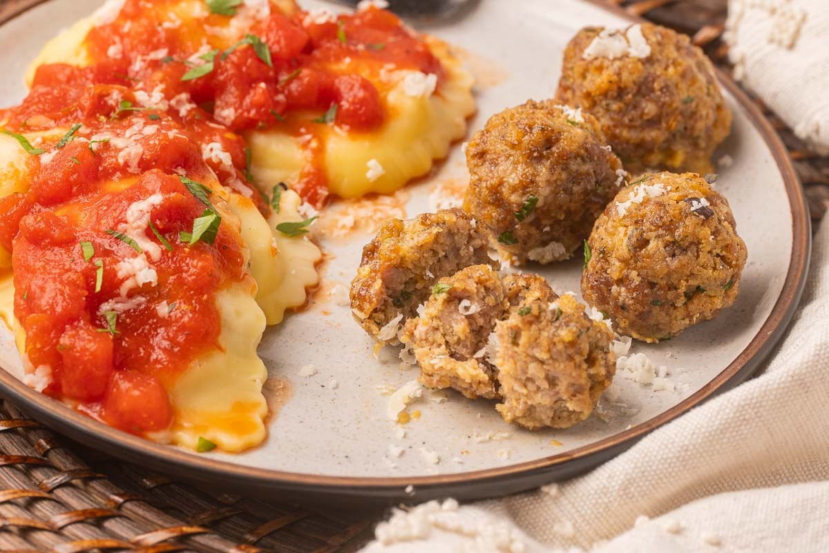 baked sausage meatballs with ravioli and sauce on plate.