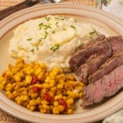 Sour cream and chives mashed potatoes, sliced steak, corn on plate.