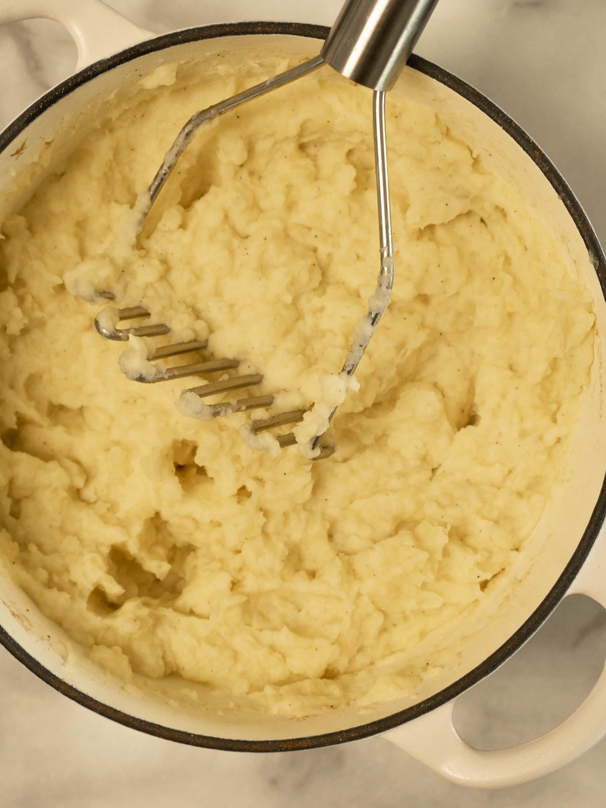 Potatoes with a masher in pot.