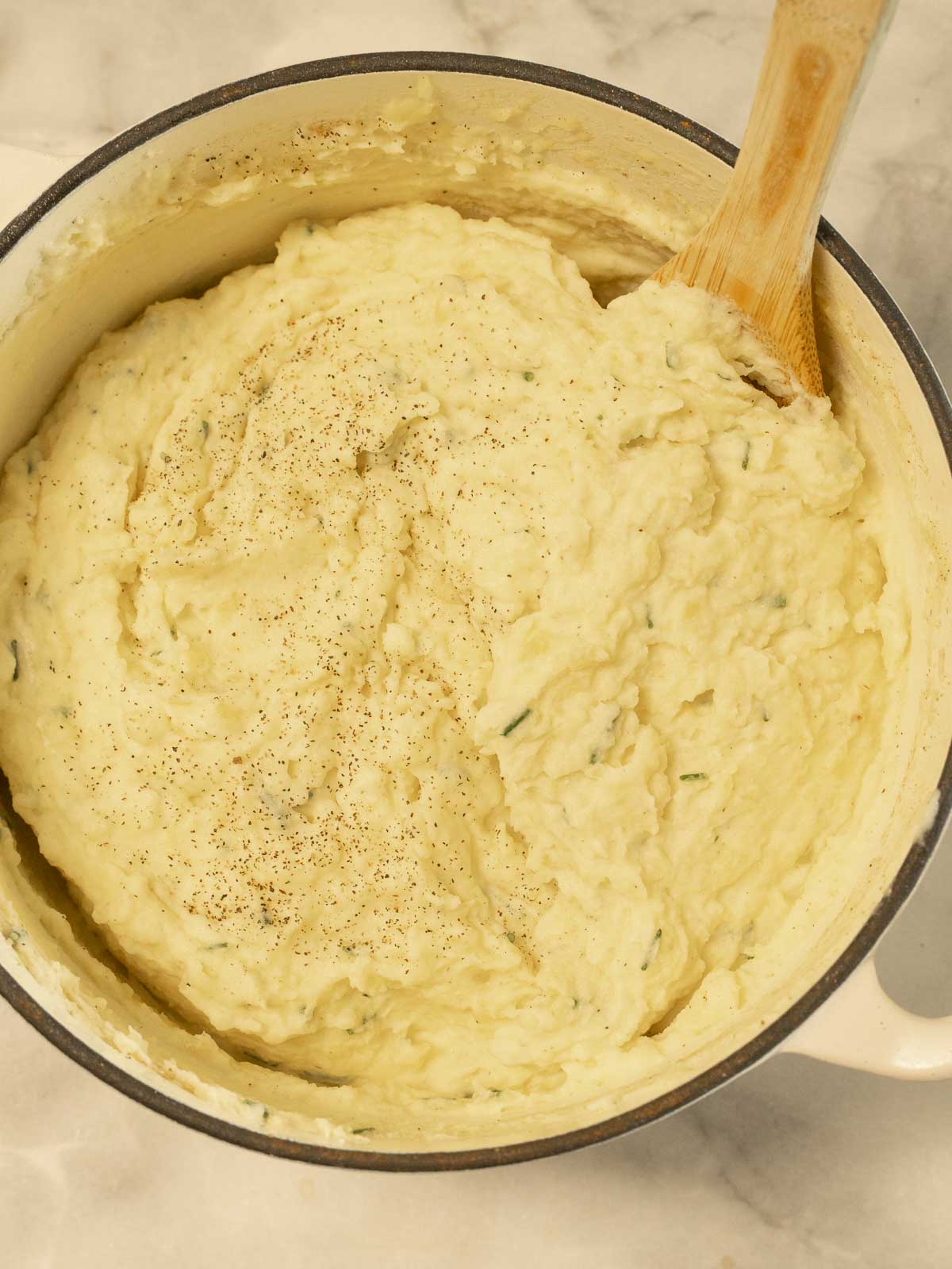 Mashed potatoes stirred in large pot.