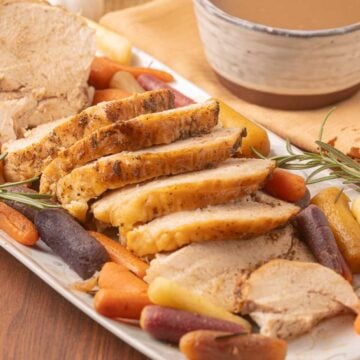 Roasted Turkey breast and carrots, rosemary and sage on platter with bowl of gravy.