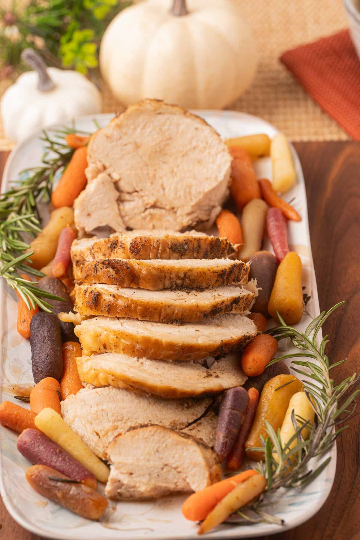 Sliced boneless turkey breast with carrots and herbs on platter.