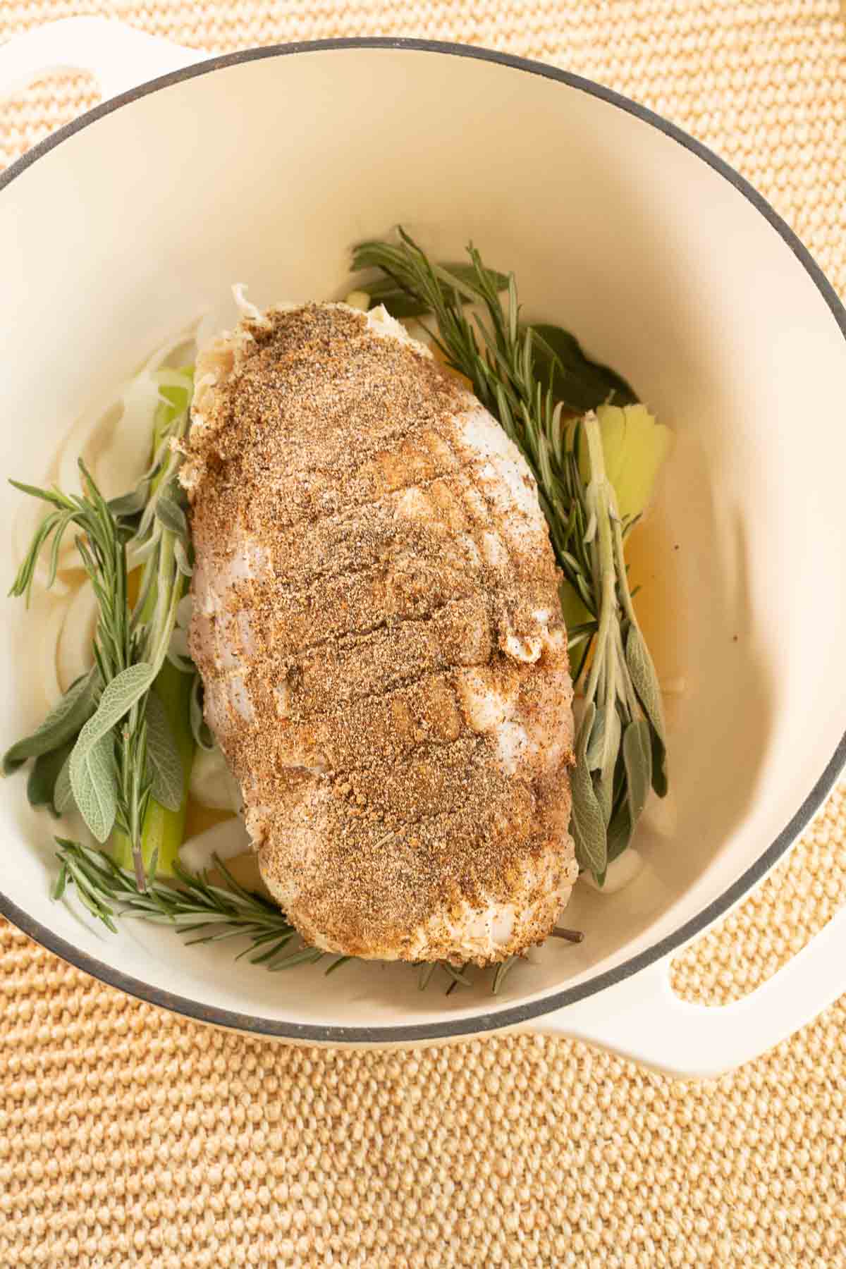 Seasoned boneless turkey breast, vegetables and herbs in pan.