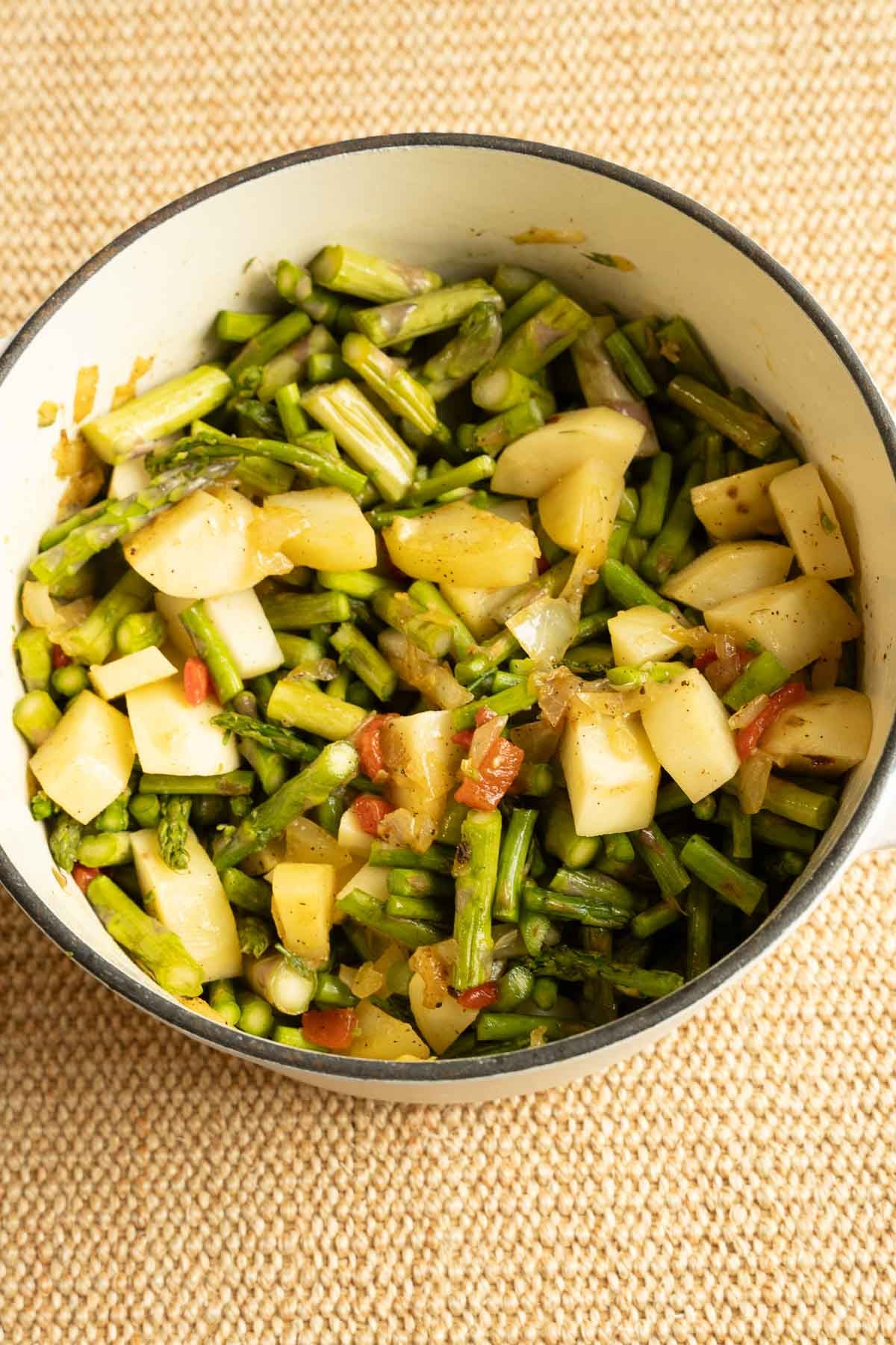 Asparagus, potatoes, red pepper, garlic in large white pot.