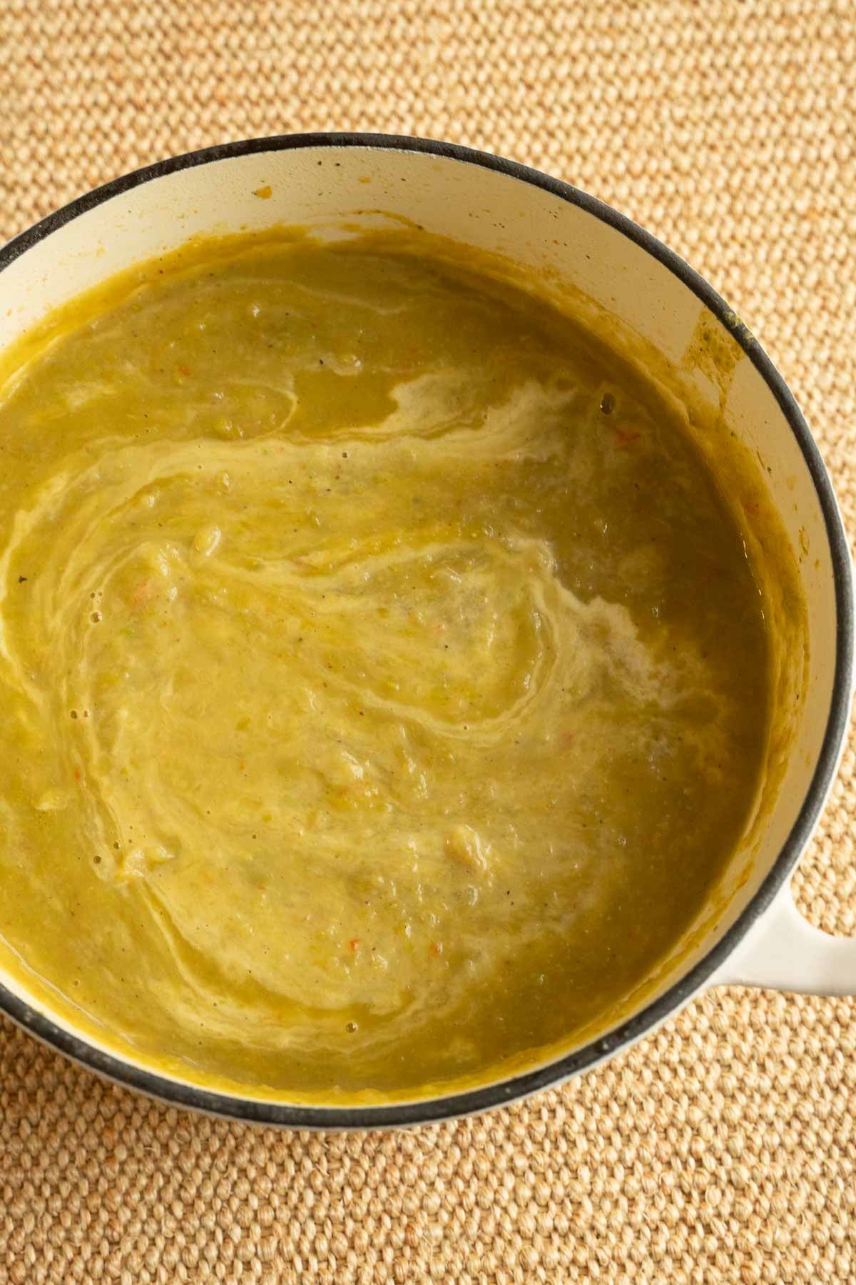 Cream of Asparagus and Potato soup with drizzle of heavy cream on top in pot.