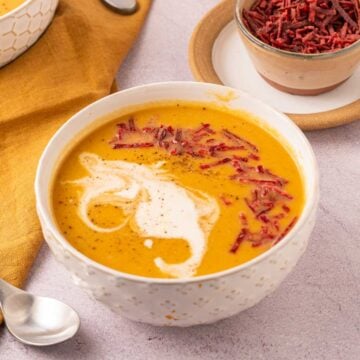 Bowl of carrot and sweet potato soup garnished with dried red beet strips.