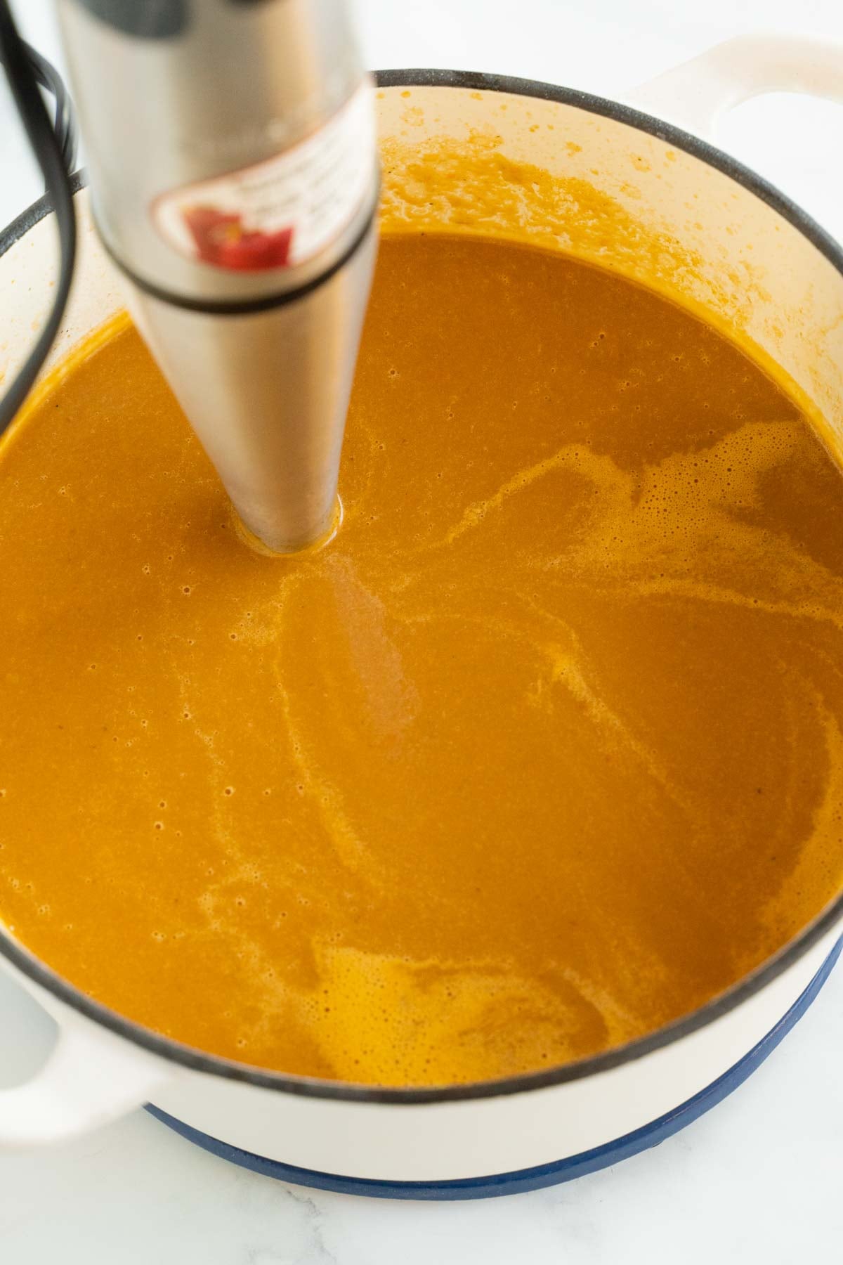 Immersion blender pureeing carrot and sweet potato soup.
