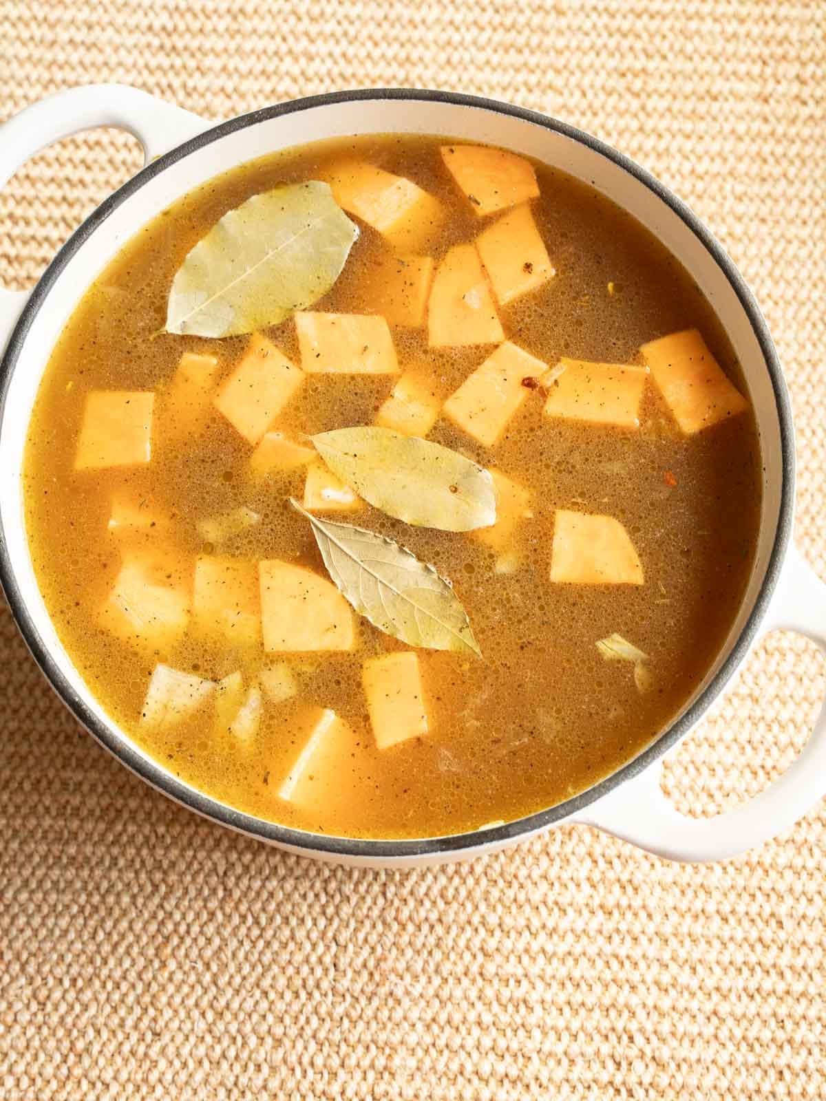 Carrots, sweet potatoes, onion, bay leaves and broth in large pot.