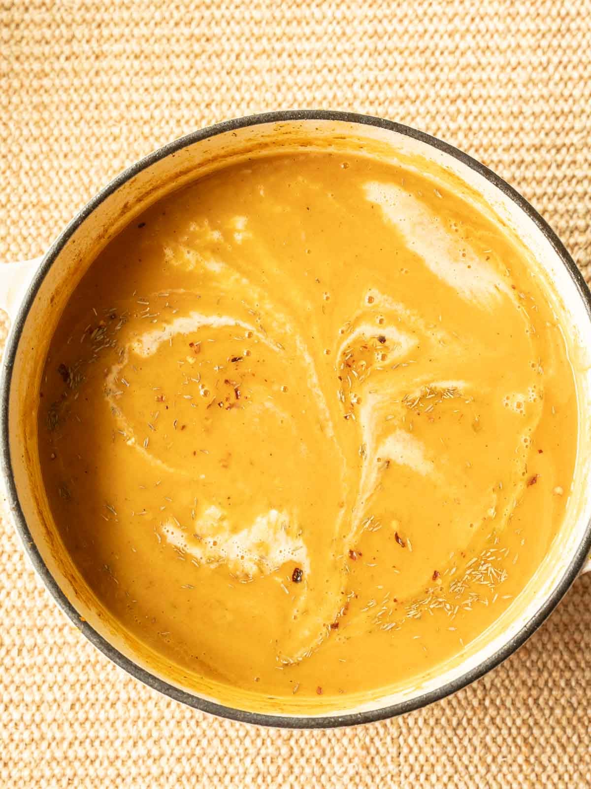 Pureed Carrot and Sweet Potato Soup in Dutch Oven with heavy cream drizzle.