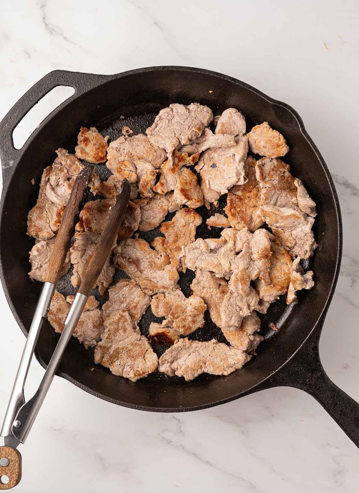 Pork tenderloin browning in cast iron skillet.