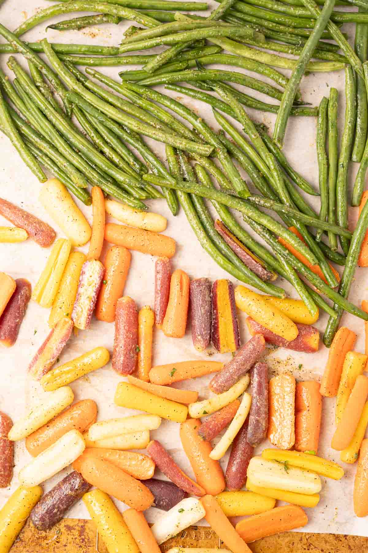 Seasoned carrots and green beans on baking tray.
