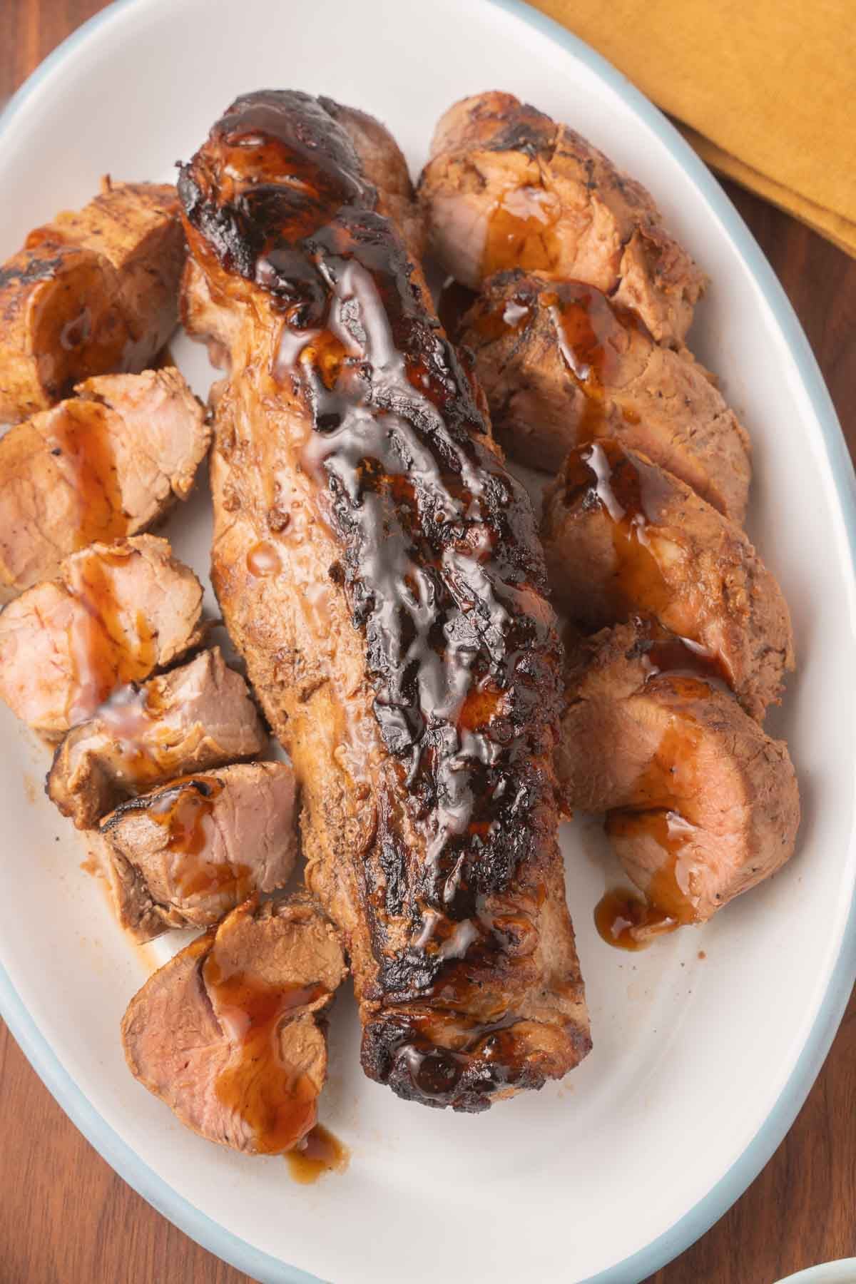 Pork tenderloin on platter with sauce drizzled on top.