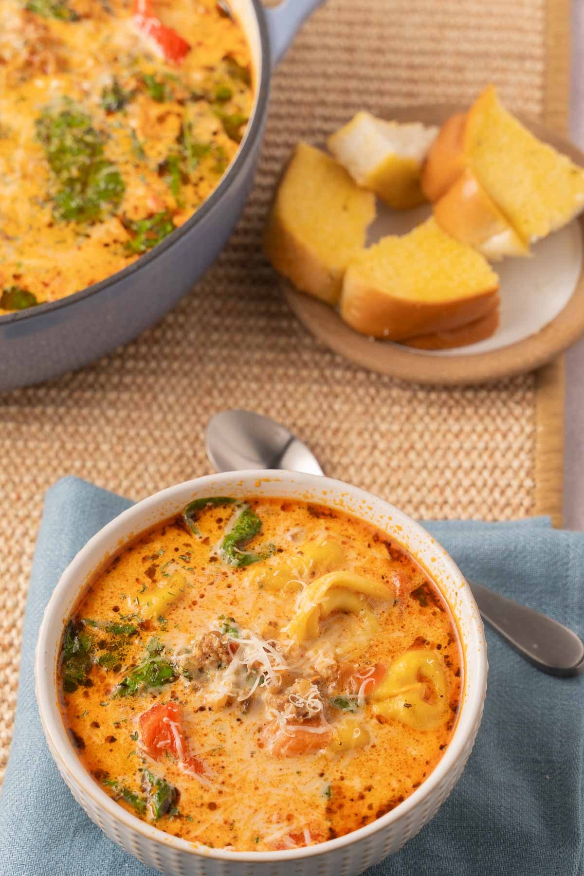 Bowl of Sausage Tortellini soup with spinach with garlic bread on plate.