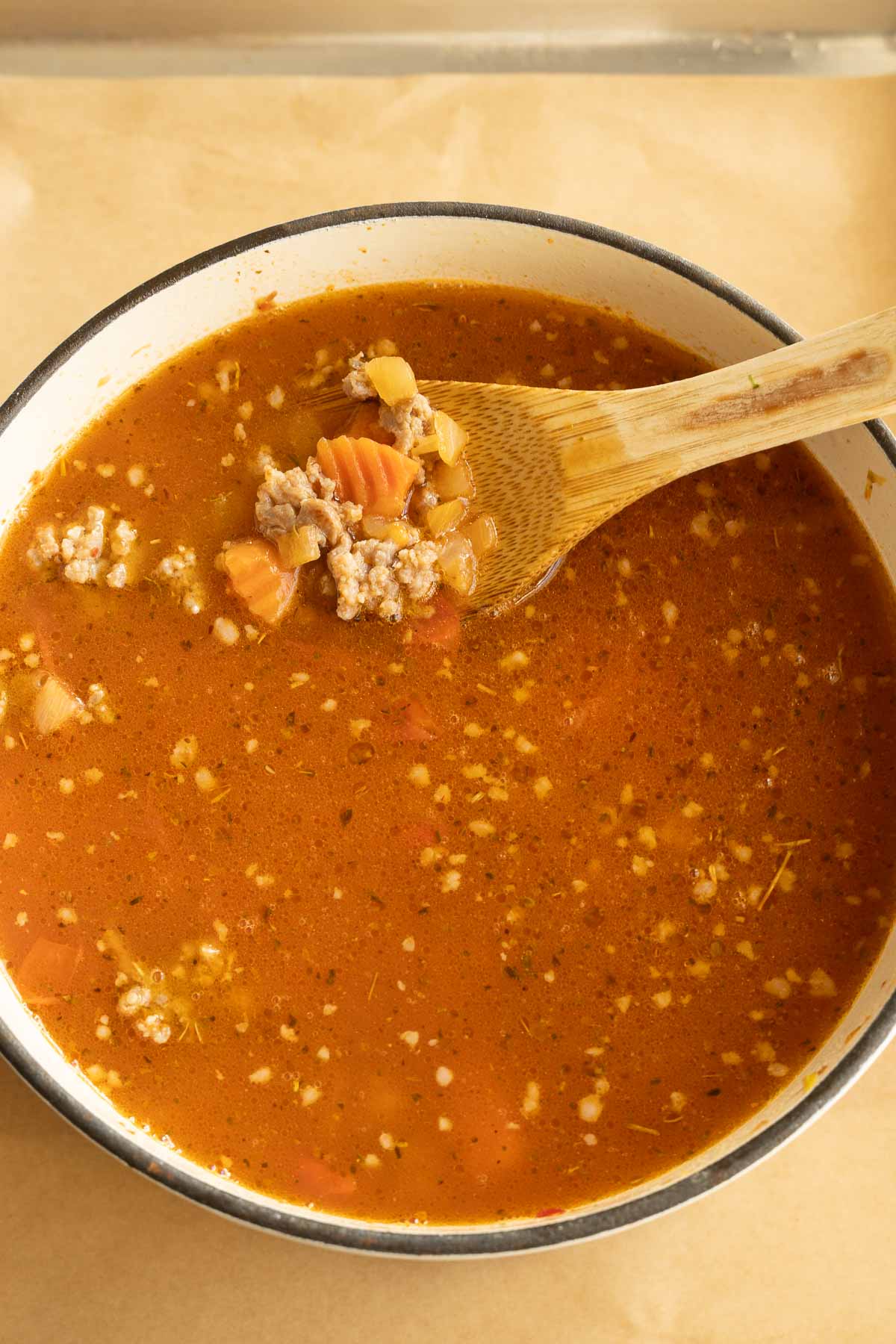 Broth added to vegetables and sausage in pot.