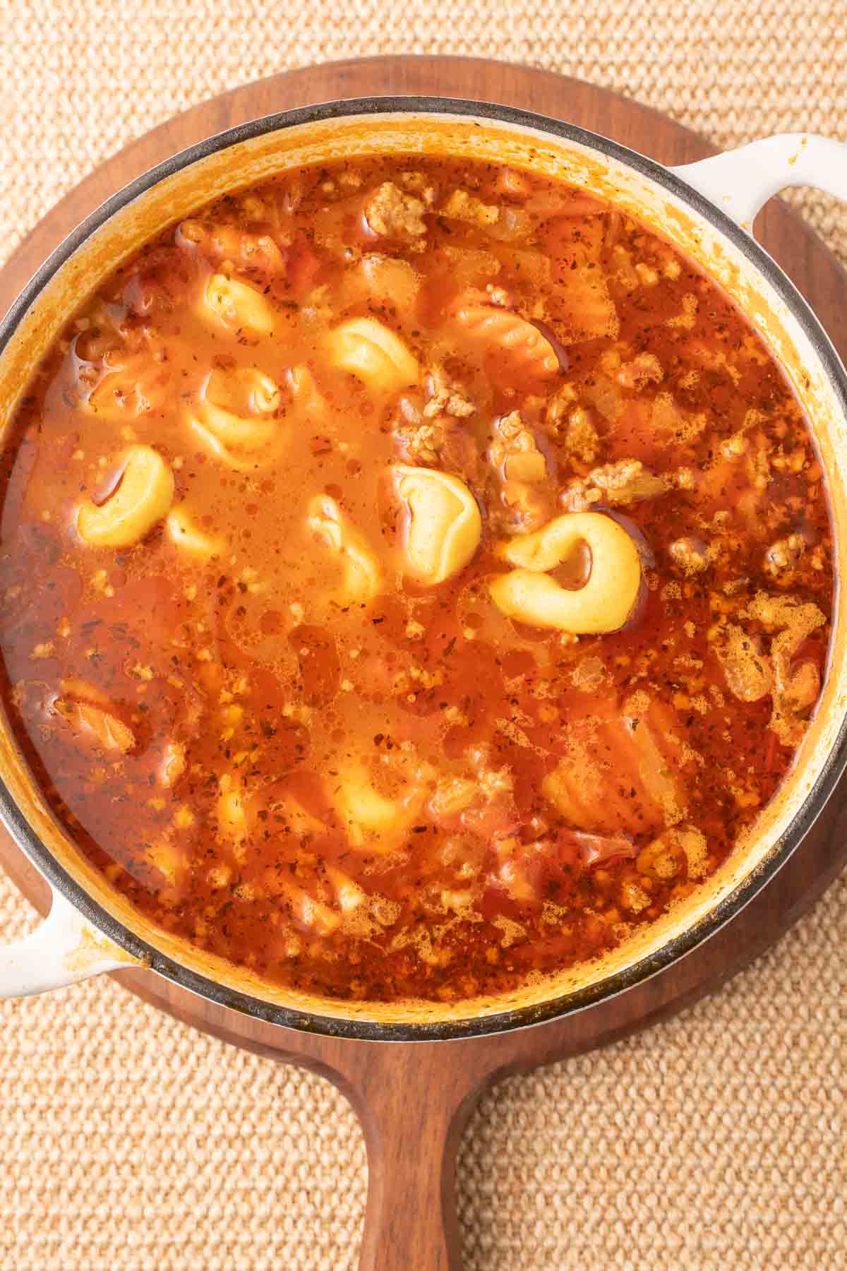 Cheese tortellini with broth, sausage and vegetables in pot.