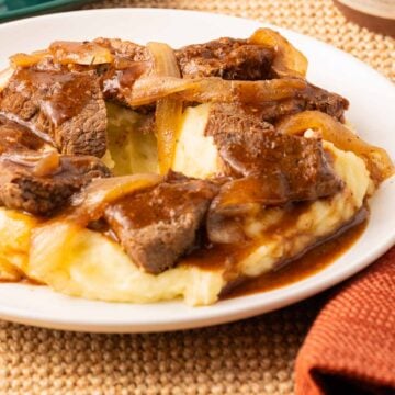 Slow Cooker Sirloin Steak and gravy over mashed potatoes on plate.