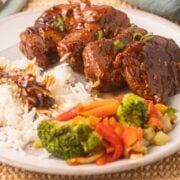 Medallions of pork tenderloin with rice, sauce and mixed vegetables on plate.