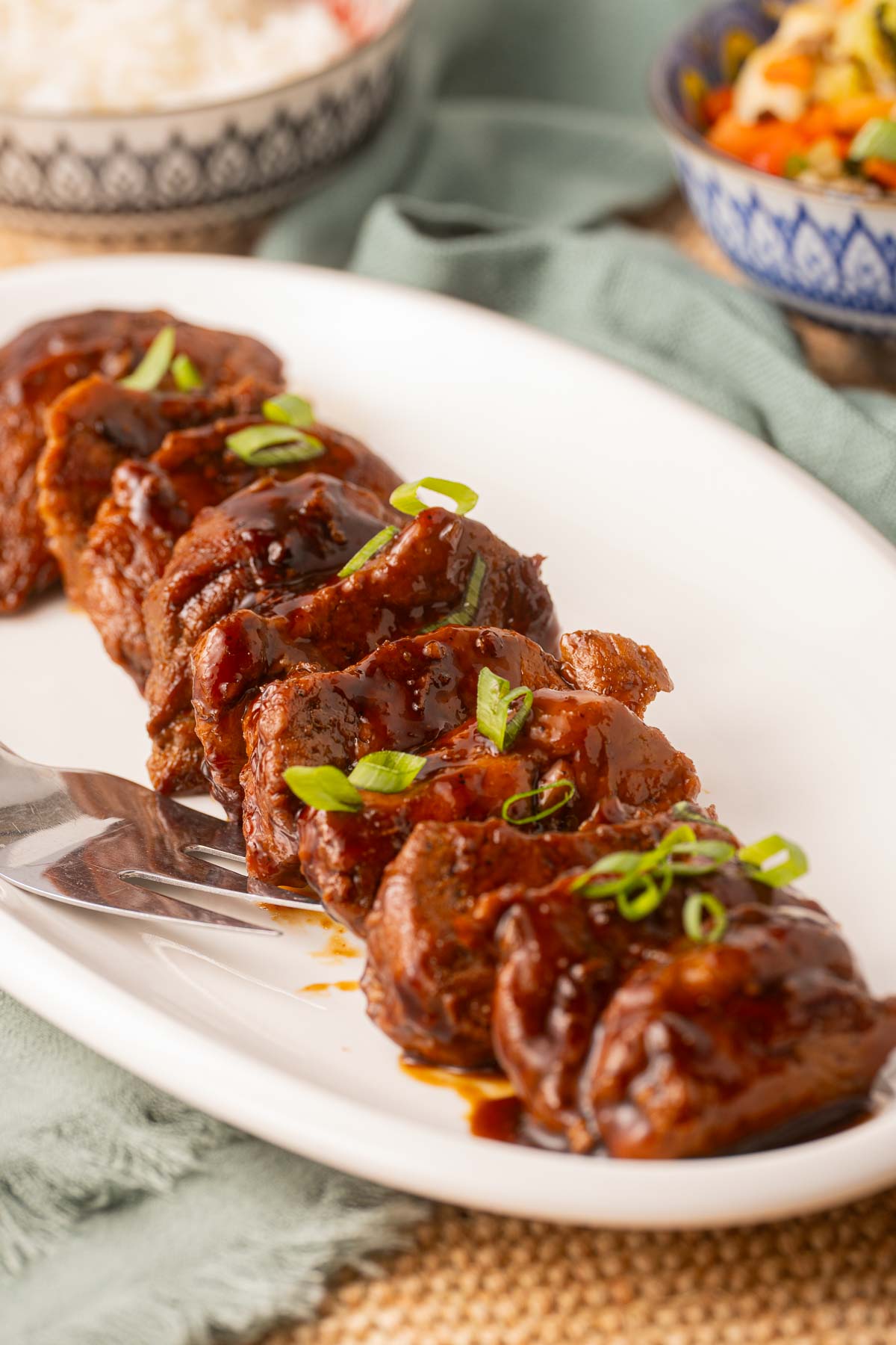 Pork tenderloin medallions on platter with rice and vegetables in bowls.