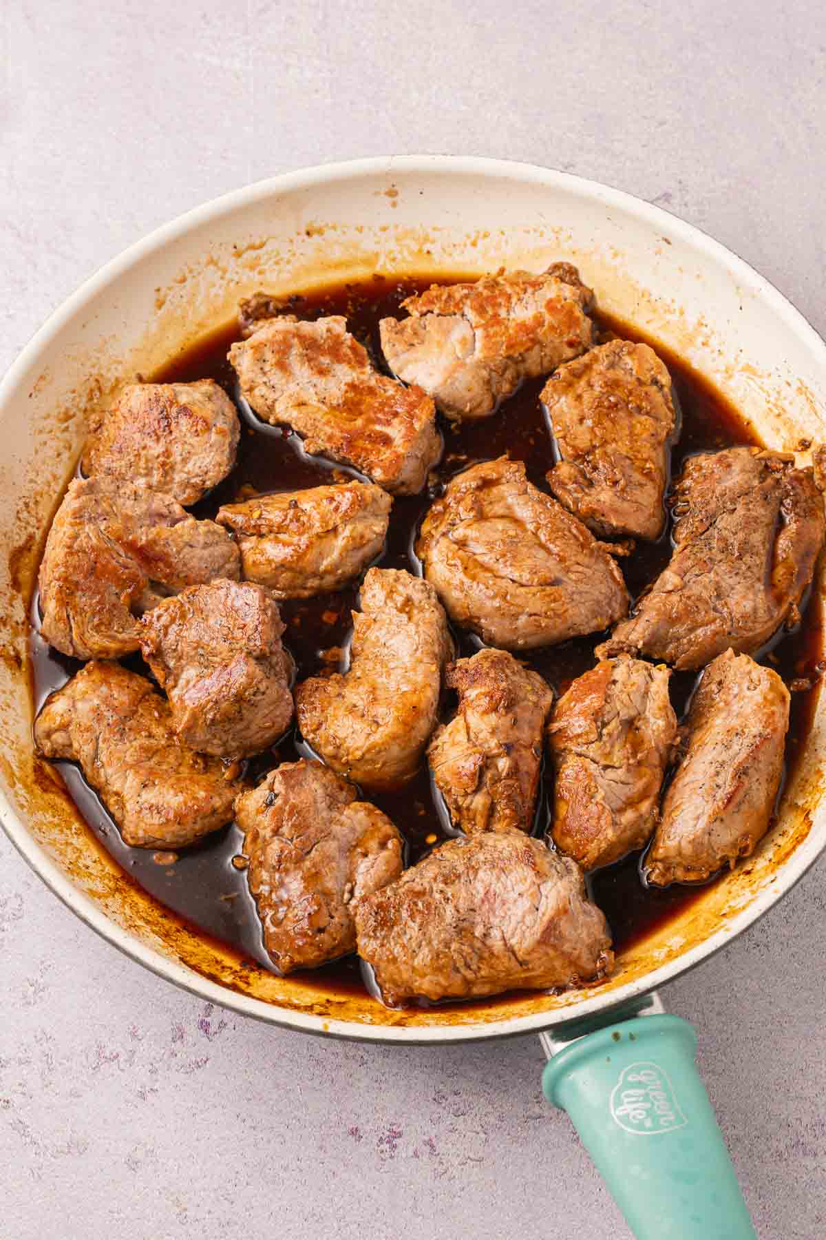 Pork tenderloin medallions simmering in sauce in skillet.