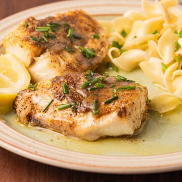 2 filets of haddock cooked in the air fryer with lemon chive sauce and egg noodles on a plate.