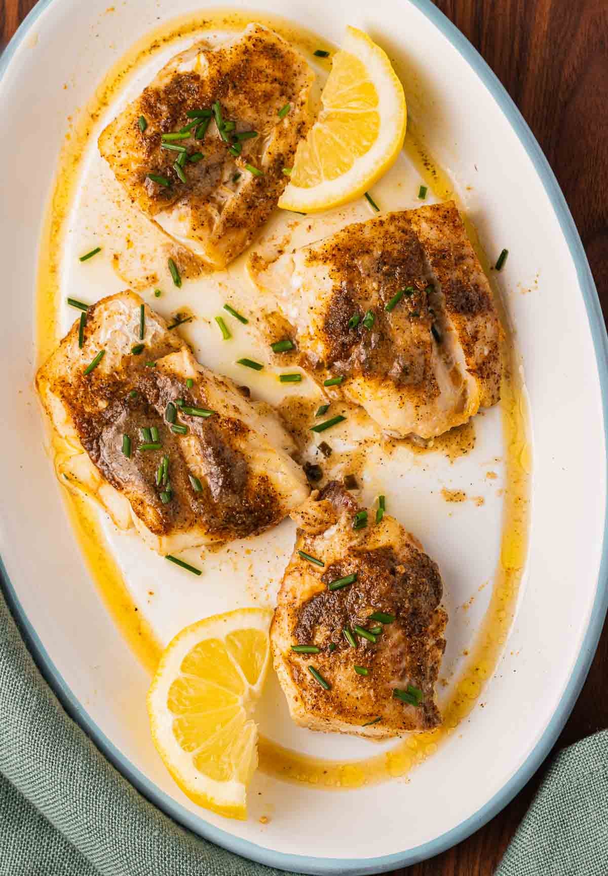 4 Air fried Haddock filets with lemon chive sauce on white platter with lemon wedges.