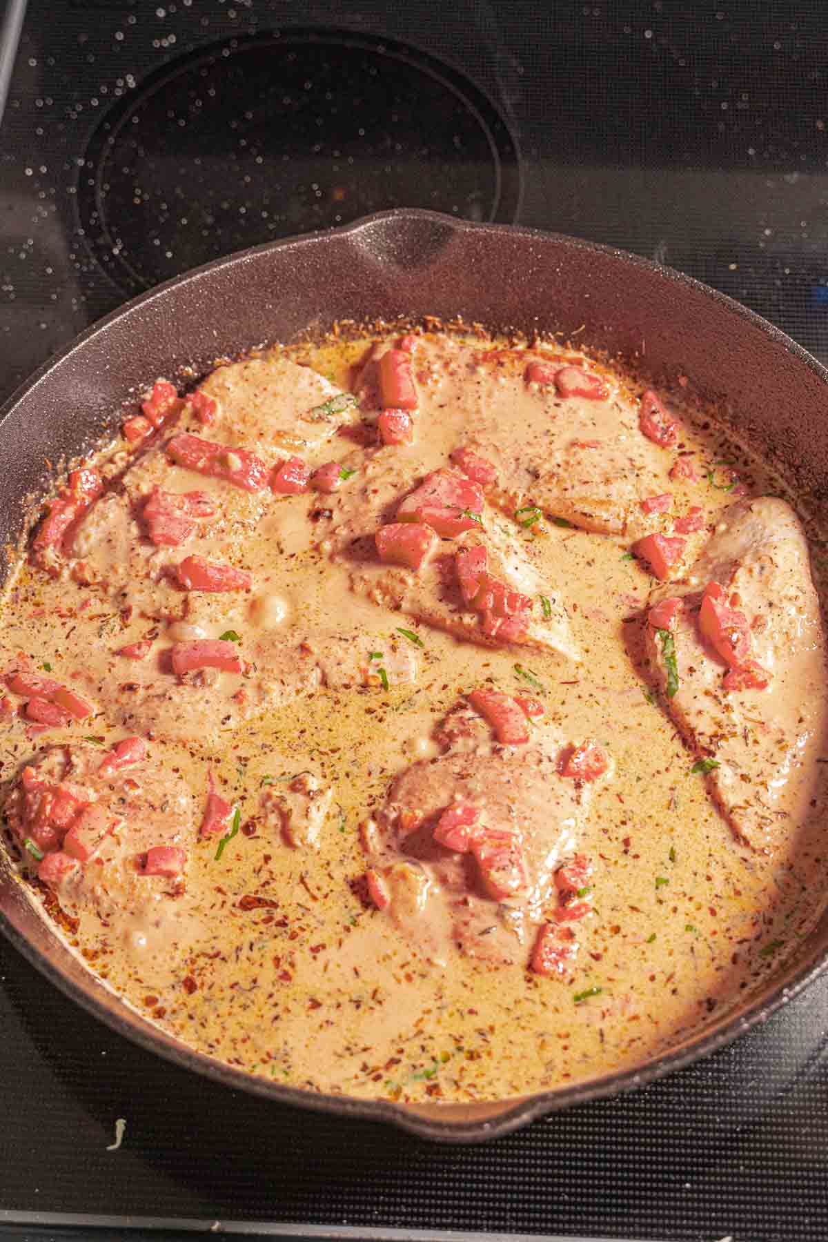 Chicken breasts in creamy red pepper and creamy sauce in skillet.