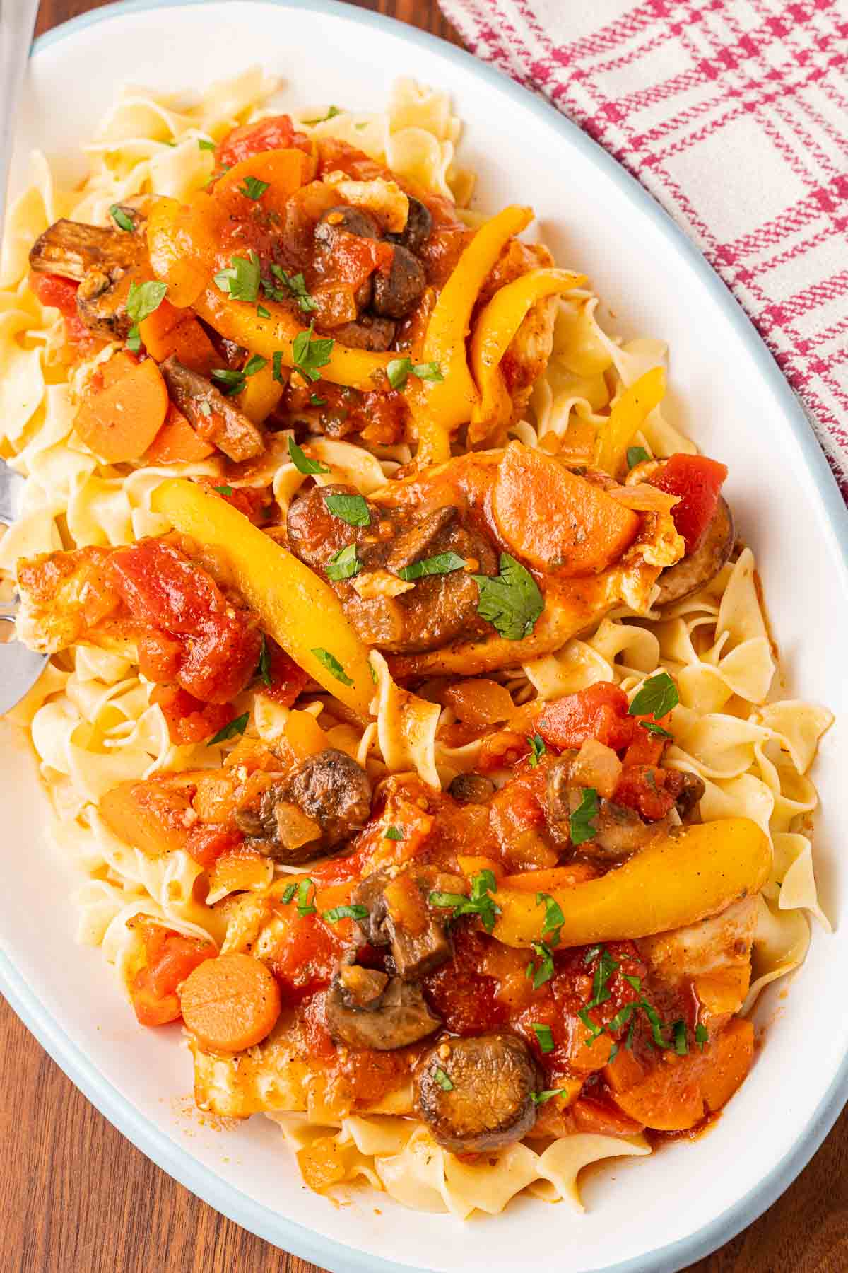 Chicken breast cacciatore over egg noodles on white platter.